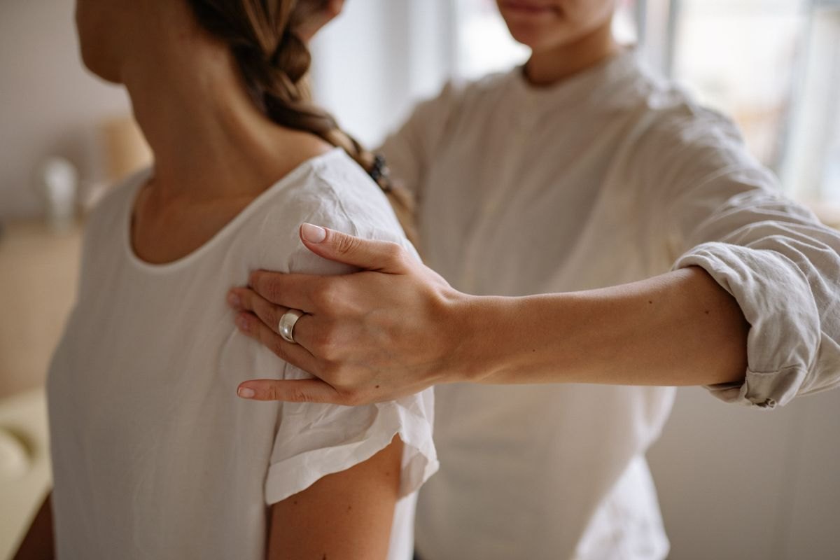 Massage therapist checking a clothed client's shoulder during an assessment before treatment begins