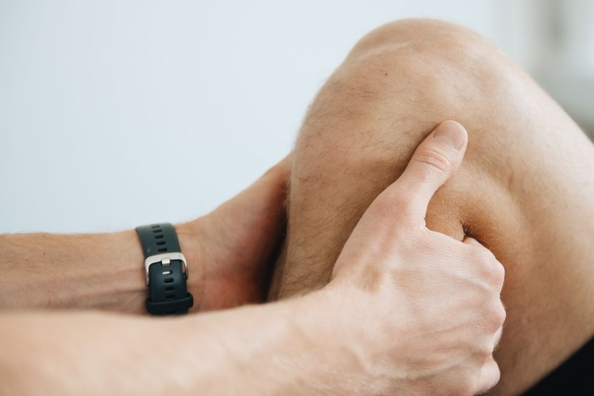 Close-up of a therapist using thumb pressure on the muscle beside a client's knee